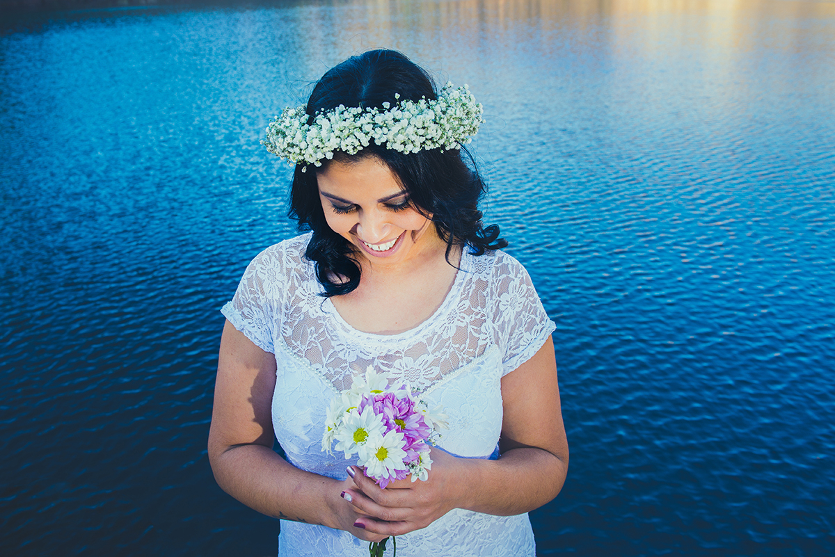 Noiva dando lindo sorriso para o seu buque de noiva com o lazo azul das Minas do camaquã ao fundo em seu ensaio pré wedding