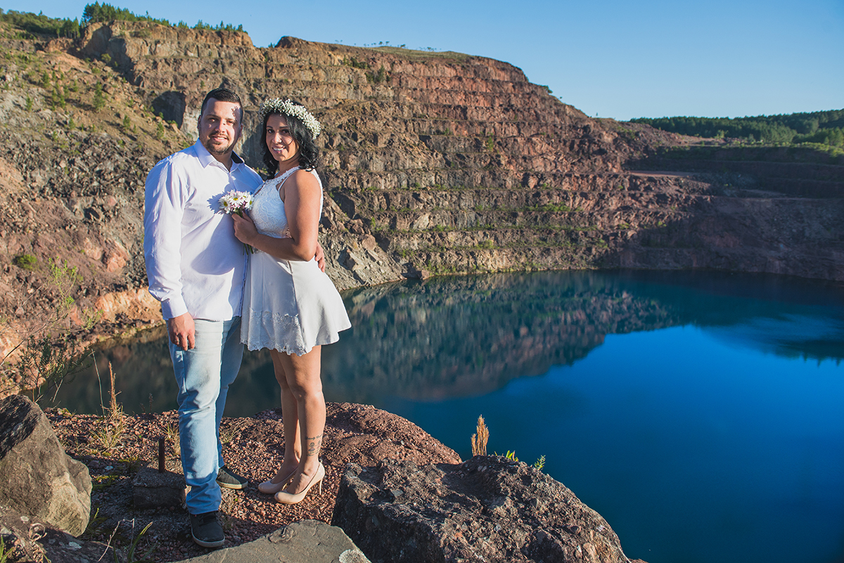 Noivos posando para foto com o lago azul das minas do camaquã ao fundo durante ensaio de casalmento pré wedding.