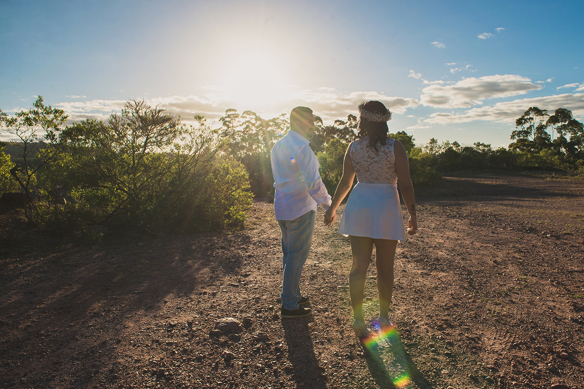 Casal de noivos, noivo de mãos dadas com a noiva andando emdiração ao por do sol durante o ensaio pré wedding realizado antes do casamento nas minas do camaquã.