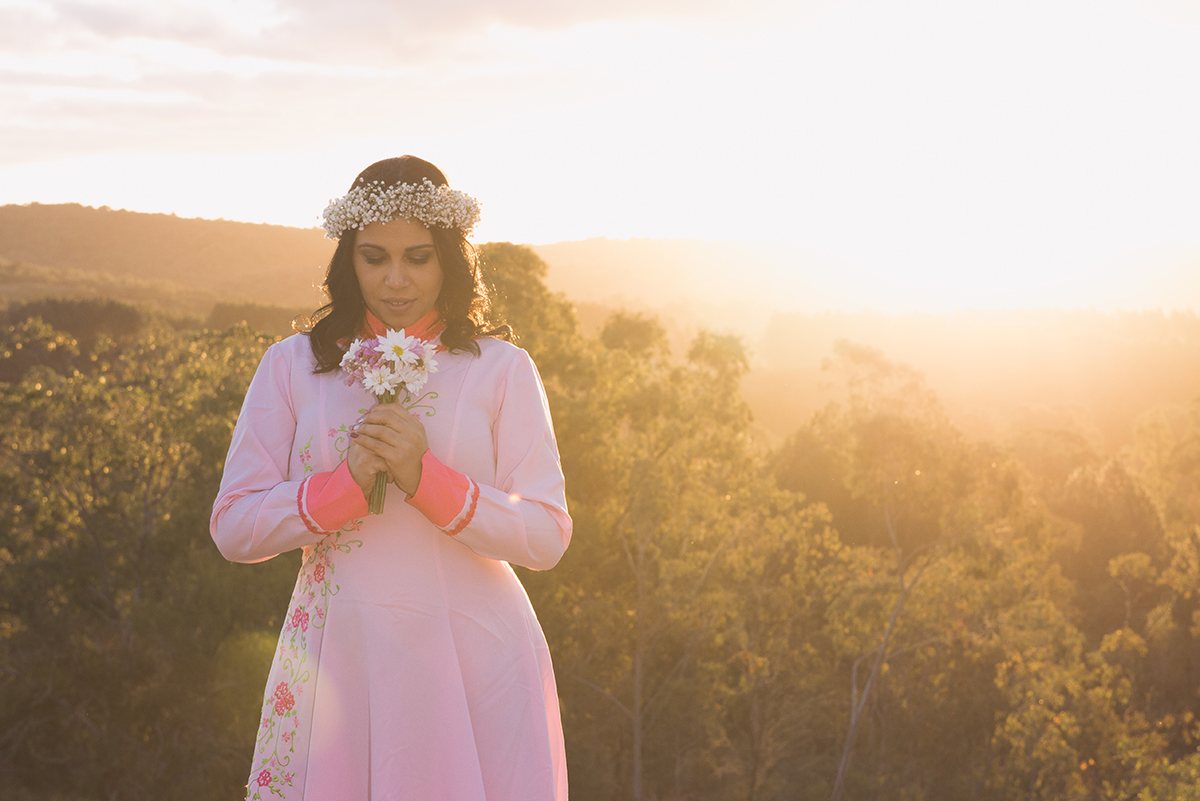 Noiva olnahdo o buque de noiva com sol ao fundo compondo esta linda foto durante o ensaio pré wedding do casal antes do casament.