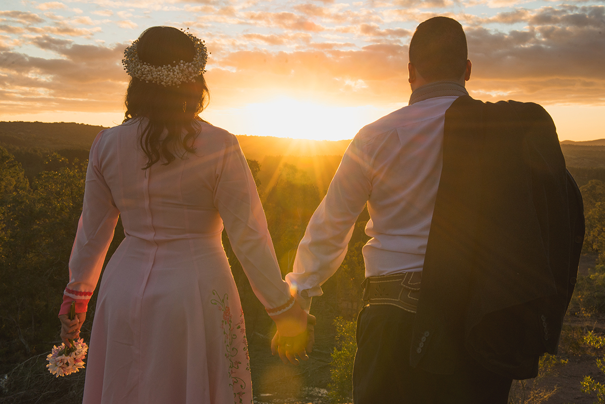 Noivo de mãos dadas com a noiva admirando o por do sol durante ensaio pré wedding antes do casamento nas minas do camaquã.