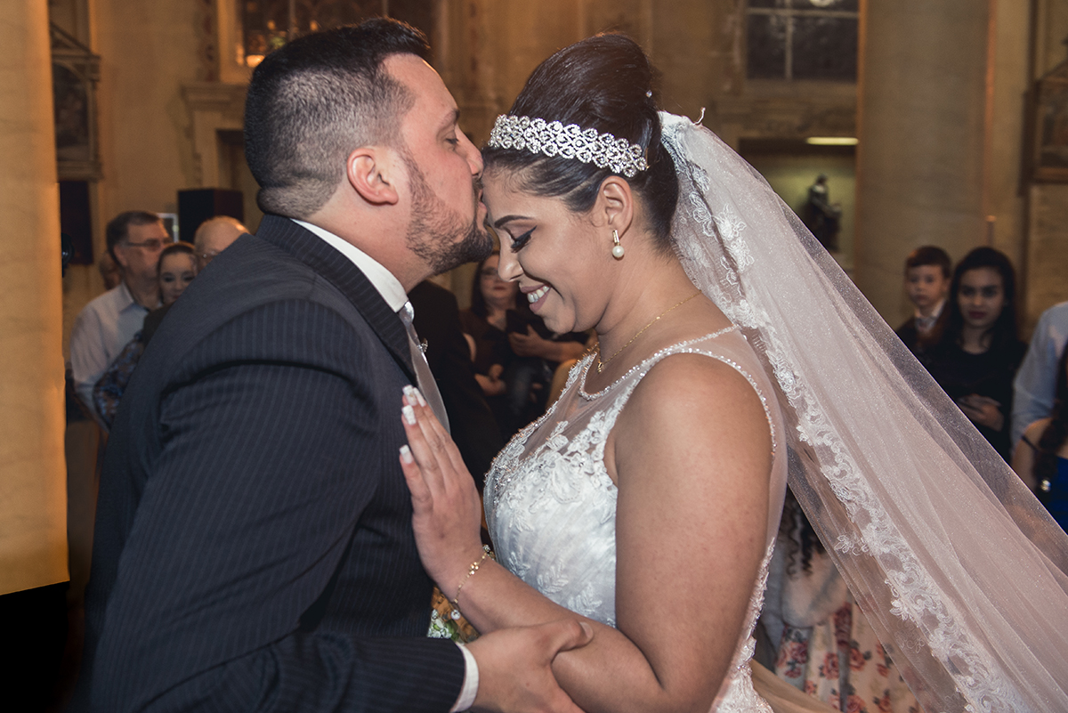 Detalhe do noivo beijando a testa da noiva no altar no dia do casamento.