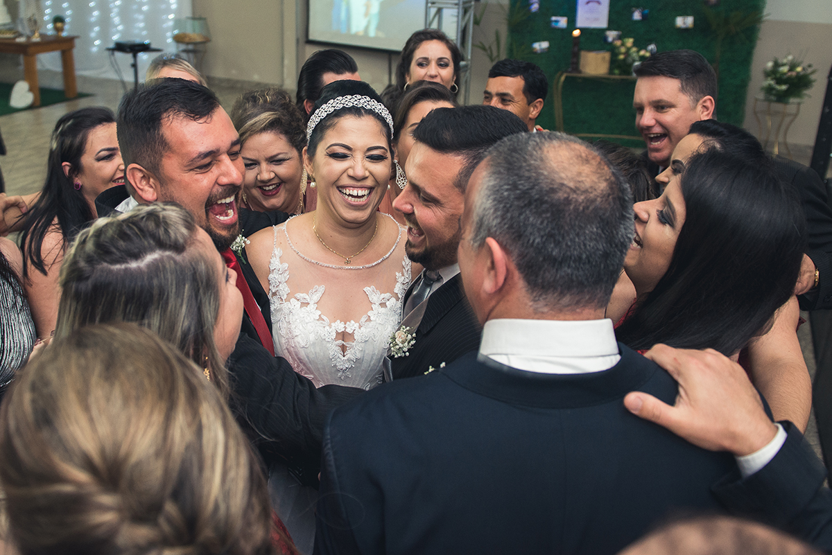 Foto dos padrinhos dos noivos todos em conjunto abraçando o casal durante a recepção do casamento.