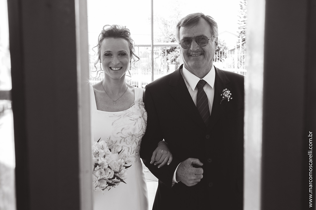 Foto em preto em branco da noiva e do pai na porta de igreja momentos antes do casamento. Foto por Marco Moscarelli