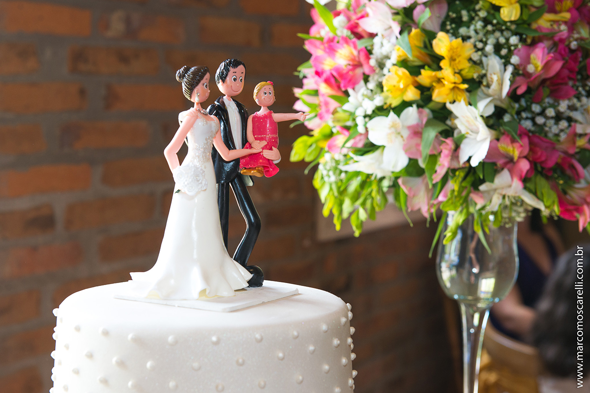 Mesa do bolo linda decorada com flores, does e um lindo casal de noivos no topo do bolo. Foto por Marco Moscarelli