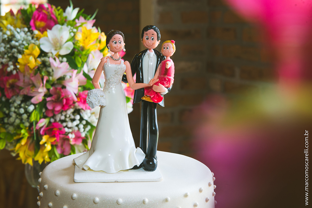 Mesa do bolo linda decorada com flores, does e um lindo casal de noivos no topo do bolo. Foto por Marco Moscarelli