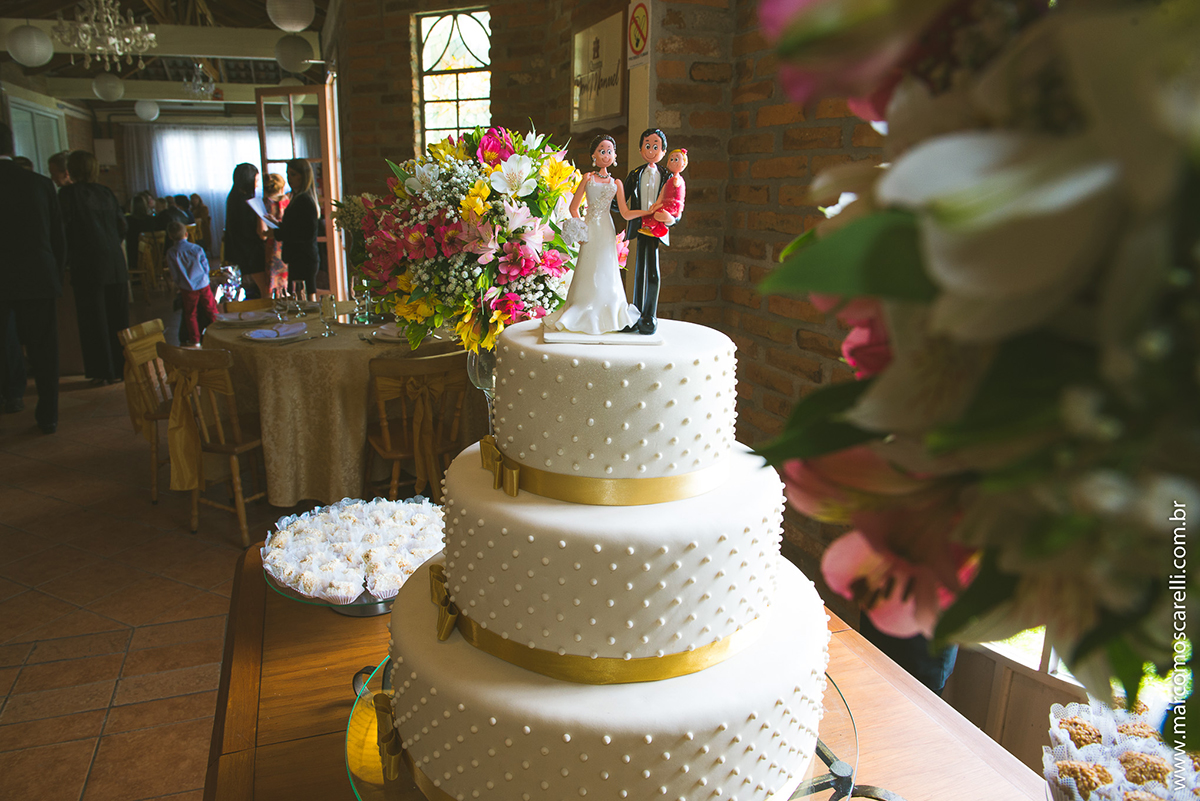 Mesa do bolo linda decorada com flores, does e um lindo casal de noivos no topo do bolo. Foto por Marco Moscarelli