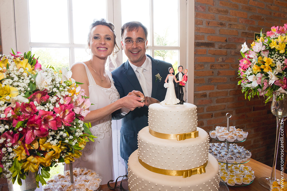 Mesa do bolo linda decorada com flores, does e um lindo casal de noivos no topo do bolo. Foto por Marco Moscarelli