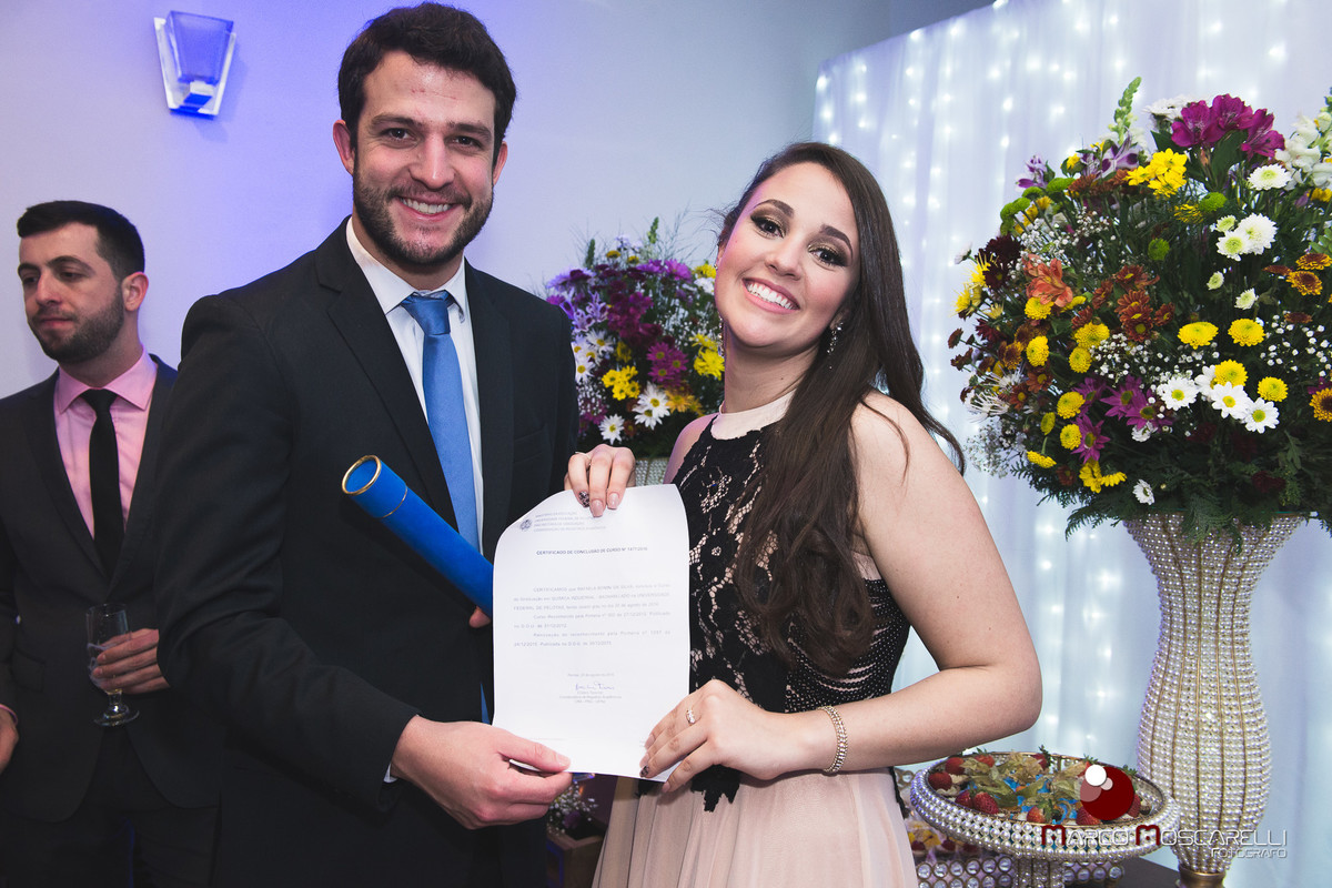 Formanda com lindo sorriso posando junto a convidado, com seu diploma de formartura. Foto por Marco Moscarelli
