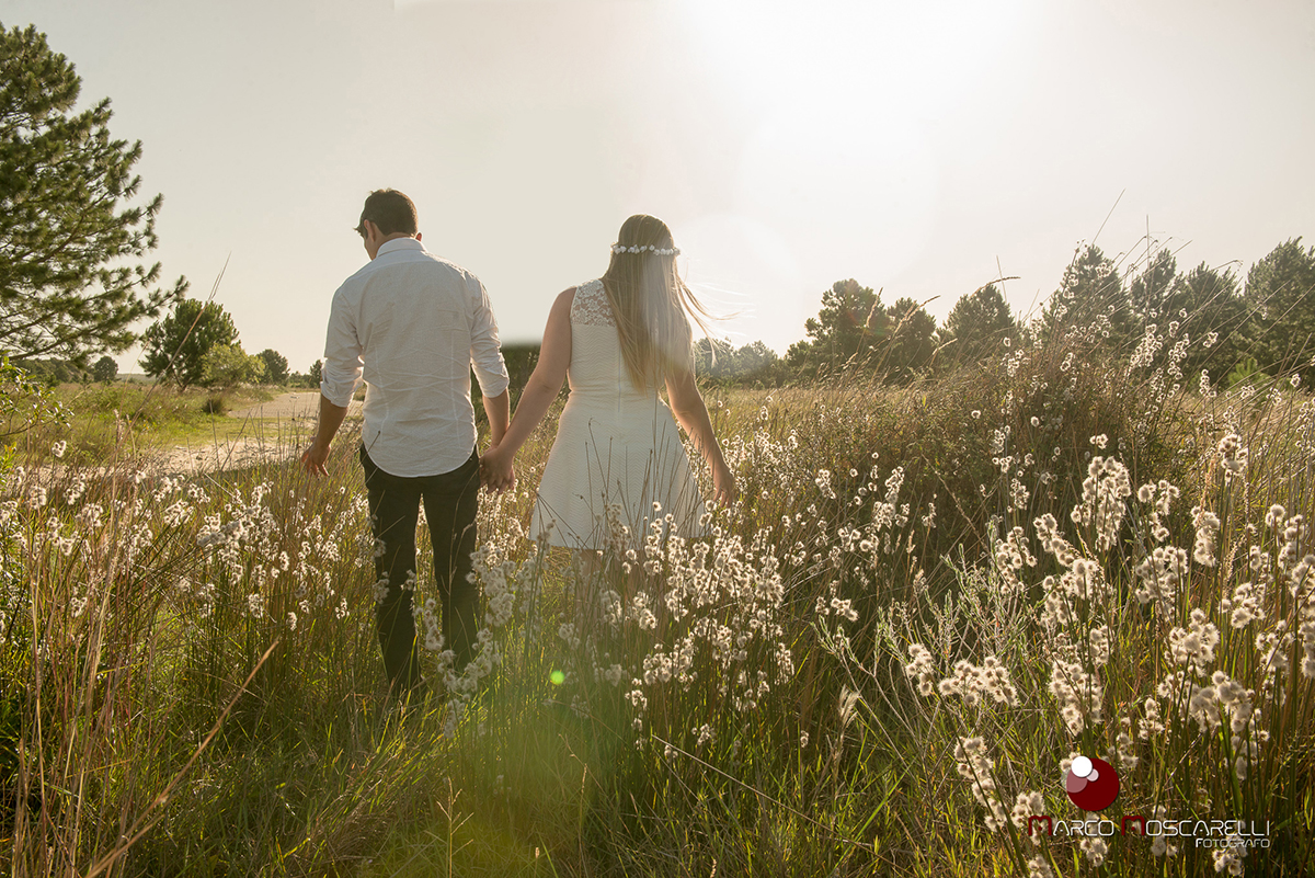 Casal de noivos caminhando no por do sol em um lindo campo acariciando a vegetação durante ensaio pré-wedding. Foto por Marco Moscarelli