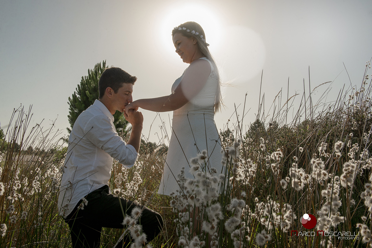 Noivo beijnado a mão da noiva em um campo durante o por do sol durante ensaio pré-wedding. Foto por Marco Moscarelli