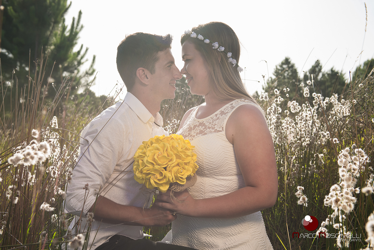 casal de noivos trocando olhares em um lindo campo florido durante por do sol em ensaio pré wedding. Foto por Marco Moscarelli