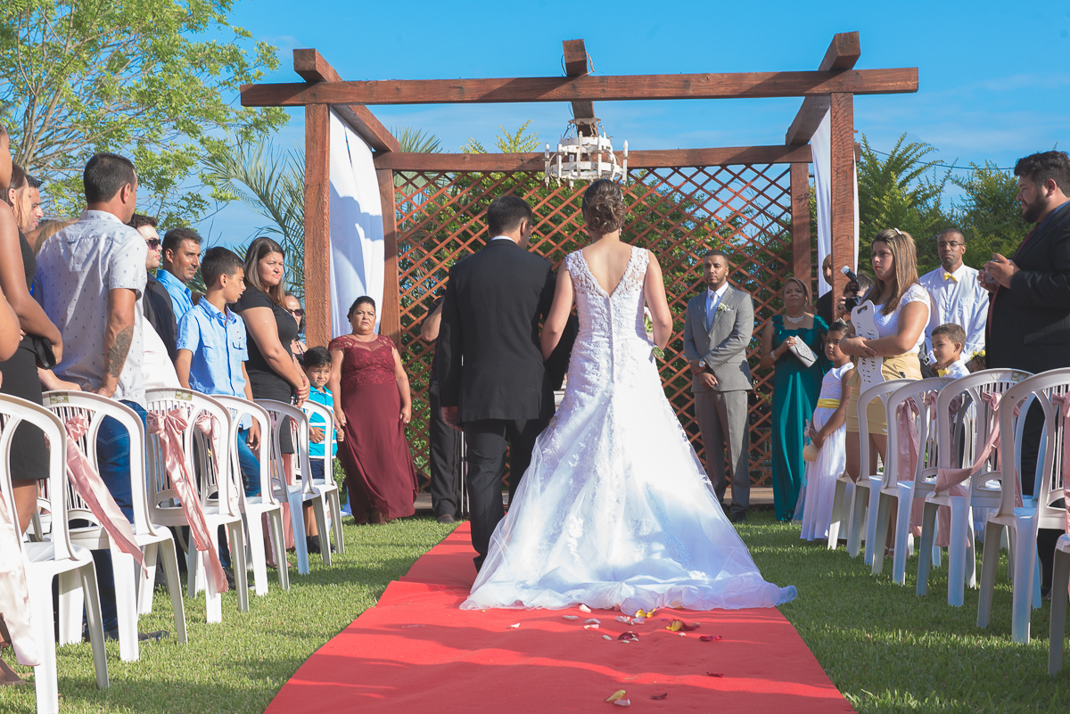 Noiva fotografada de costas indo em direção ao altar do casamento