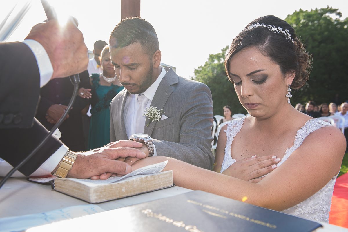 Noivos ajoelhados no altar e padre abençoando as mãos dadas dos noivos.
