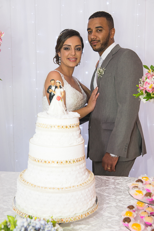 Noivos posando para fotos atras do bolo de casamento.