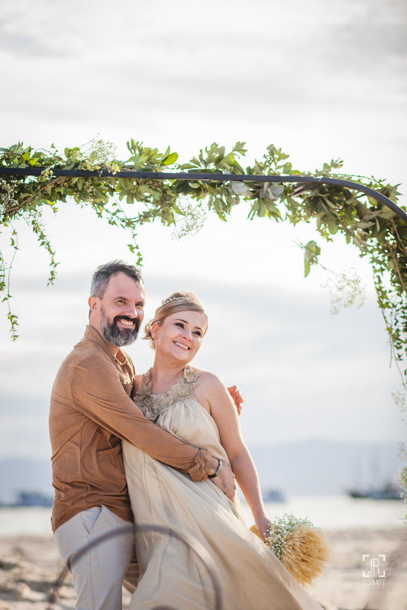 Noivos durante casamento na praia com altar de guirlanda
