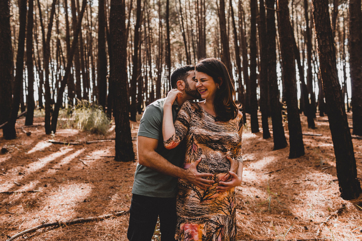Ensaio de Gestante Ana Flávia e Guilherme. Casal abraçado sorrindo em floresta. Foto feita pelo fotógrafo Gabriel Pelaquim.