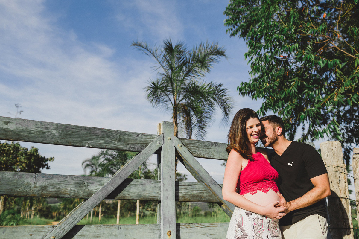 Ensaio de Gestante Ana Flávia e Guilherme. Casal abraçado sorrindo em portão de fazenda em Brasília. Foto feita pelo fotógrafo Gabriel Pelaquim.