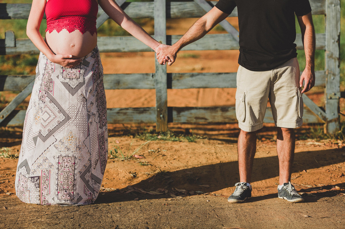 Ensaio de Gestante Ana Flávia e Guilherme. Casal de mãos dadas em portão de fazenda em Brasília. Foto feita pelo fotógrafo Gabriel Pelaquim.