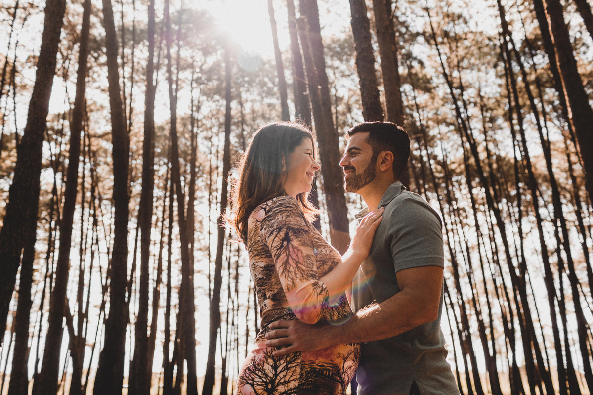 Ensaio de Gestante Ana Flávia e Guilherme. Casal abraçado sorrindo em uma floresta. Foto feita pelo fotógrafo Gabriel Pelaquim.