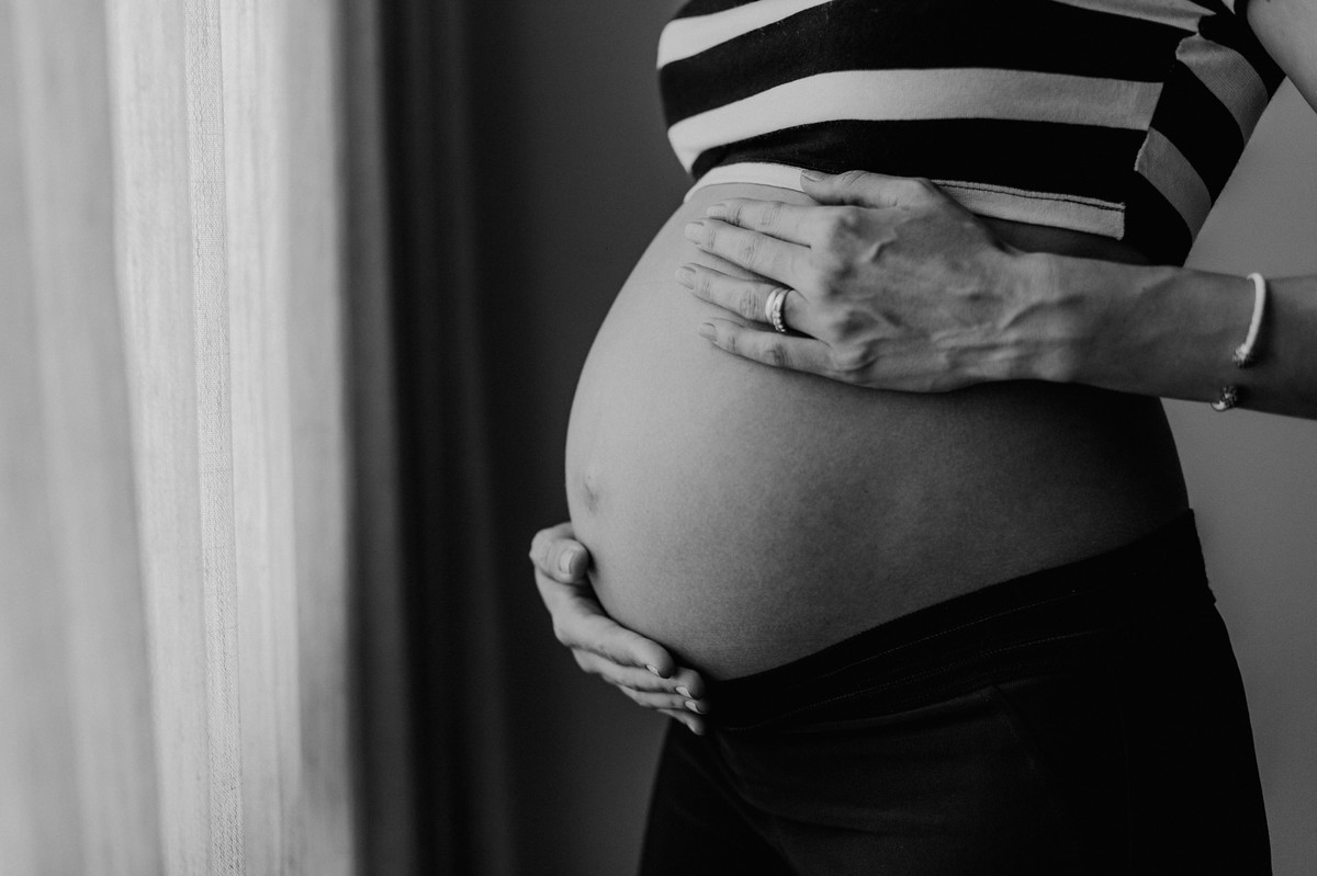 Gestante Rubia acariciando sua barriga no quarto do seu neném. Foto pelo fotógrafo Gabriel Pelaquim.