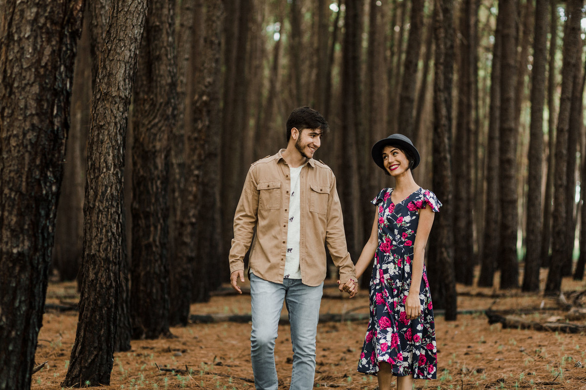 Casal de mãos dadas sorrindo em floresta de pinheiros em Brasília. Foto feita pelo fotógrafo de casamento Gabriel Pelaquim.