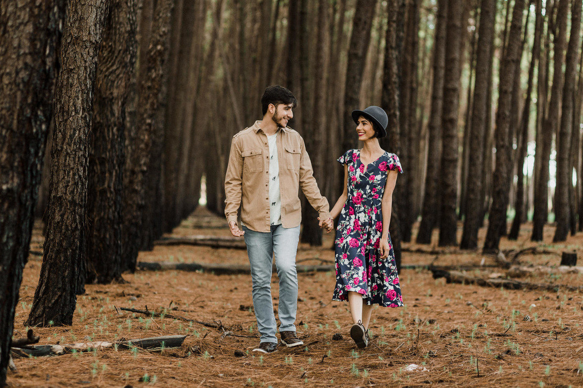 Casal de mãos dadas sorrindo em floresta de pinheiros em Brasília. Foto feita pelo fotógrafo de casamento Gabriel Pelaquim.