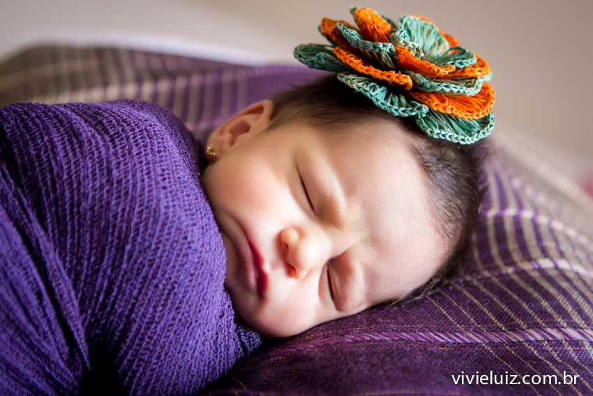 bebe enrolada com paninho roxo e laço de flor colorido