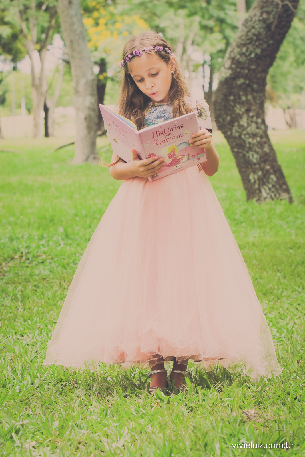 menina com vestido rosa lendo livro em parque verde
