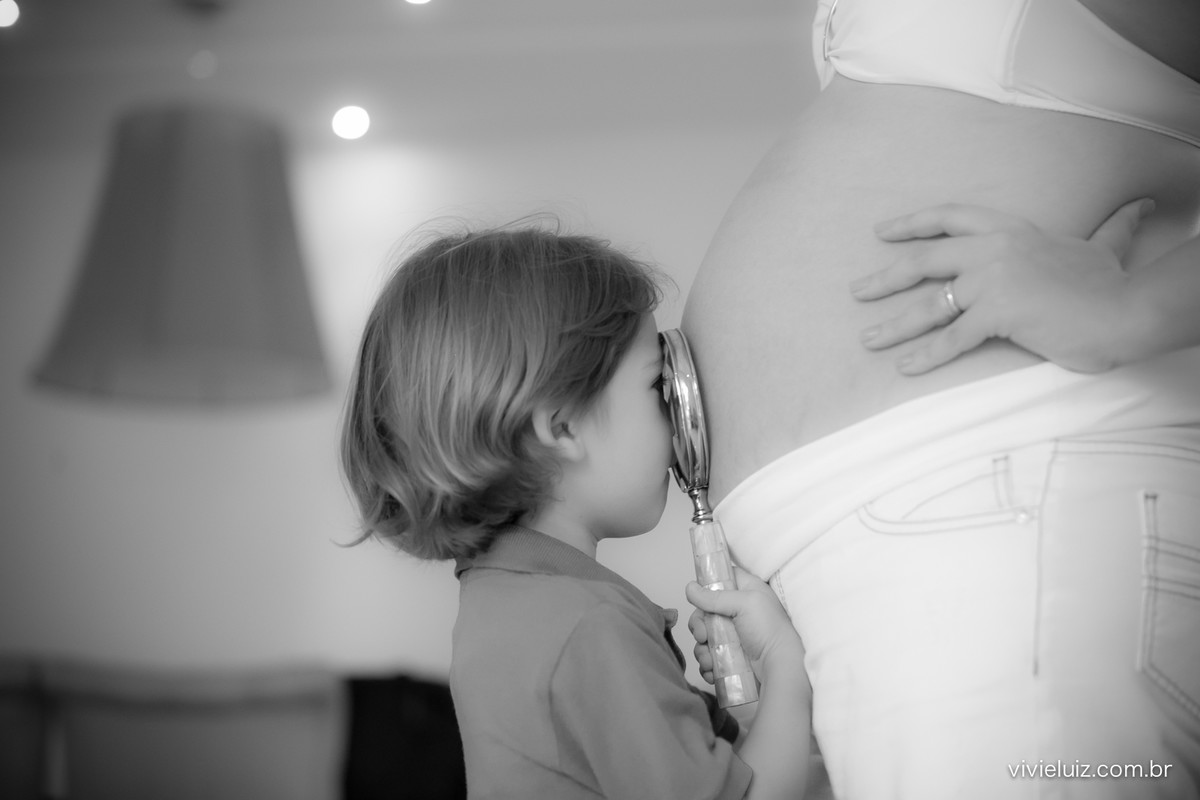 Criança olhando com lupa a barriga gestante da mãe
