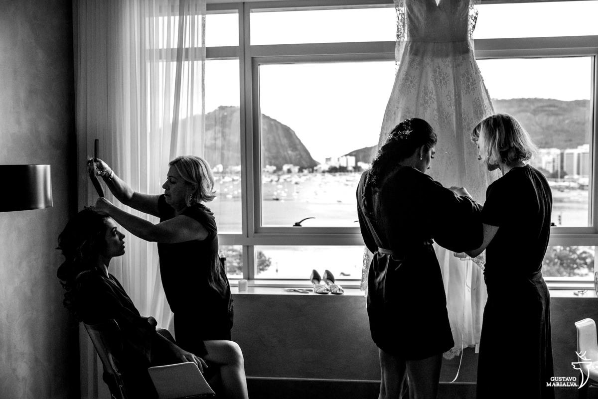 Noiva e maquiadora costurando os nomes das amigas na barra do vestido de noiva Carol Hungria