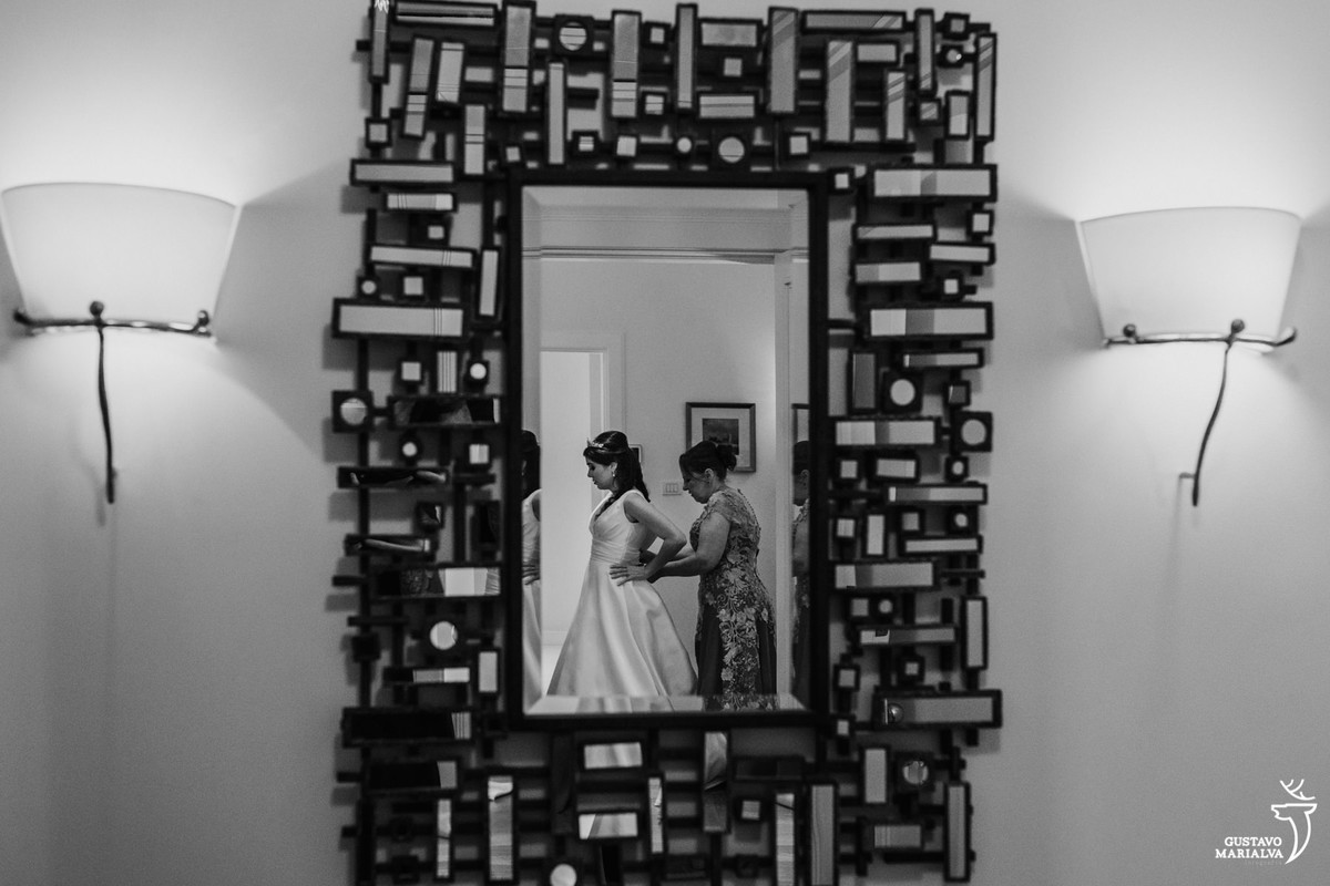 mãe da noiva fechando o vestido no reflexo do espelho na parede