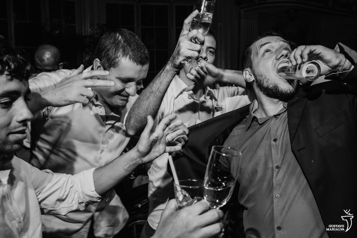 convidado coloca o copo inteiro de cerveja dentro da boca e outros amigos riem e dançam