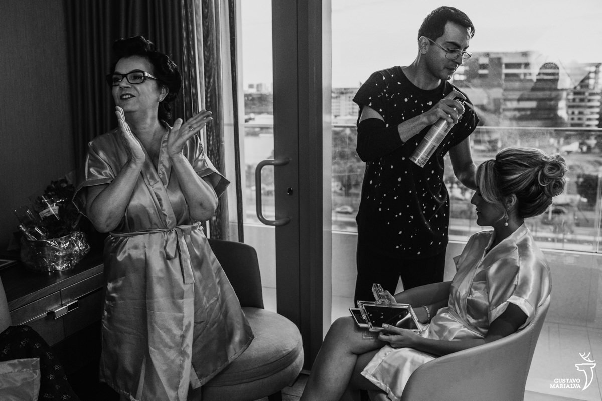 mãe da noiva aplaudindo enquanto a noiva arruma o cabelo com o maquiador daniel wagner no making of do casamento no hotel hilton no rio de janeiro