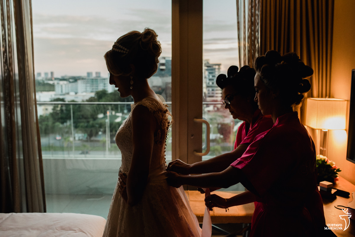 madrinha e mãe da noiva fechando o vestido de casamento da noiva no making of do casamento no hotel hilton no rio de janeiro
