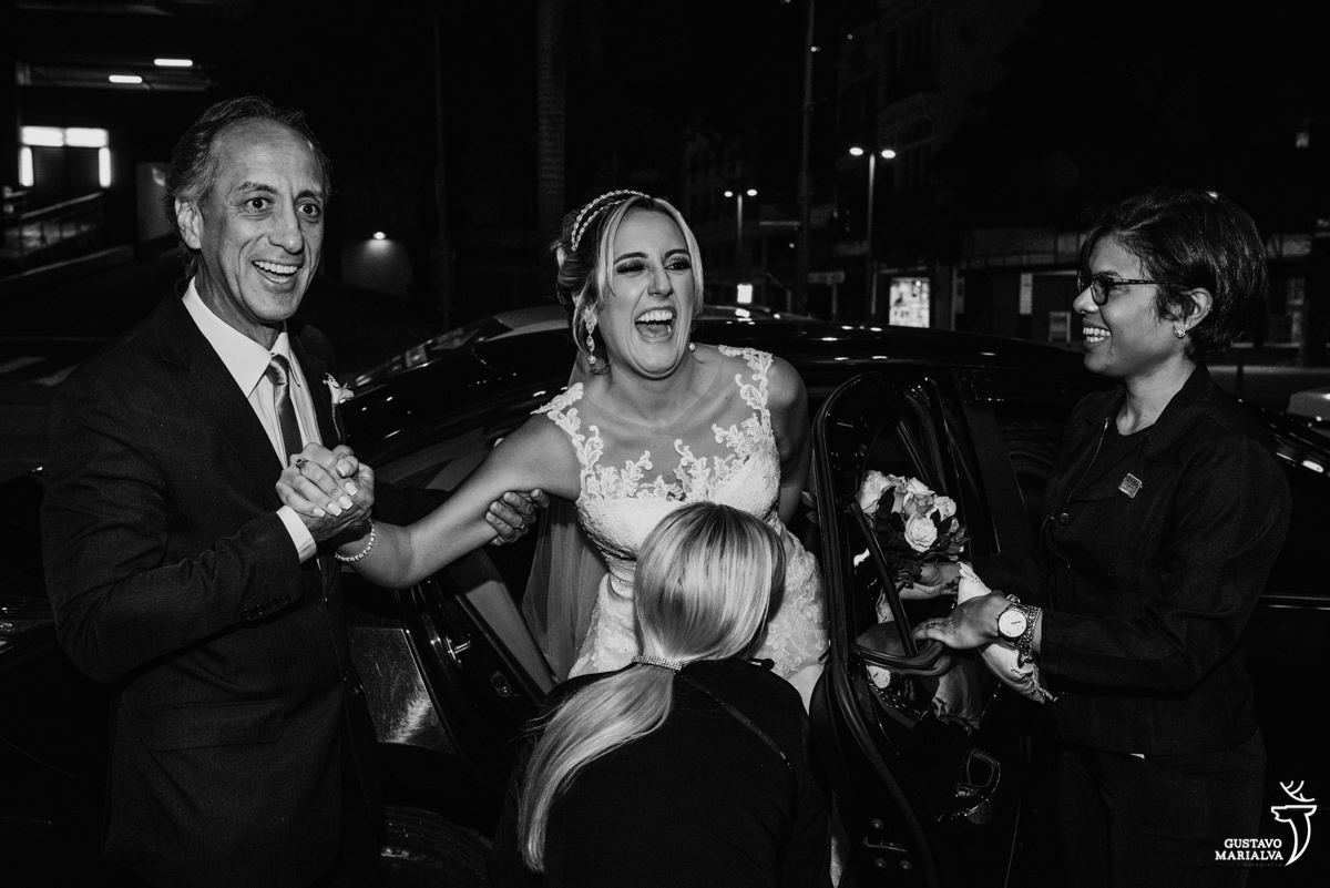 noiva sorrindo muito ao sair do carro ajudada pelo pai e por duas cerimonialistas antes de começar a cerimônia de casamento na igreja são josé no rio de janeiro