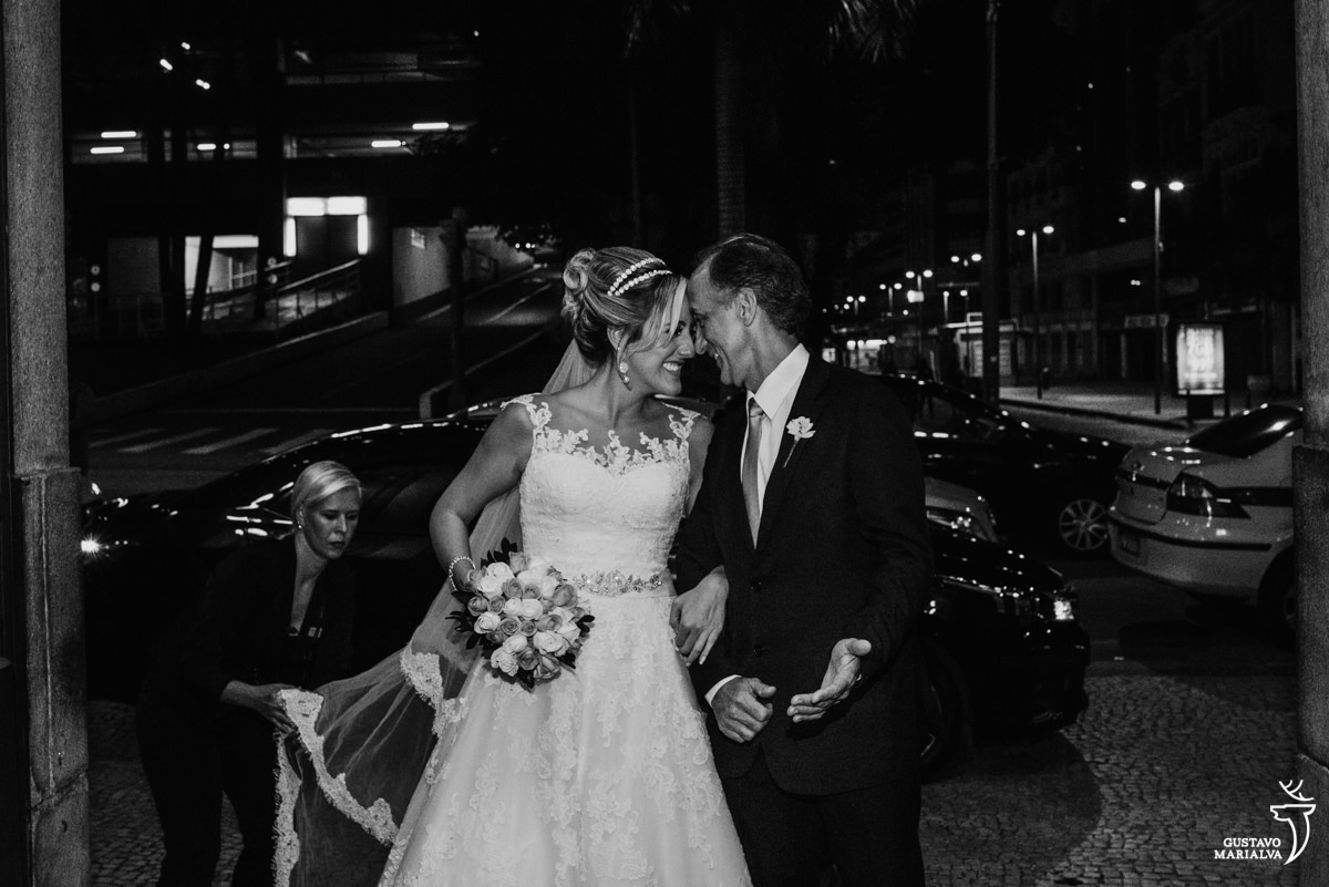 noiva e pai colando a testa e sorrindo antes de entrar na cerimônia de casamento na igreja são josé no rio de janeiro enquanto a cerimonialista arruma o vestido