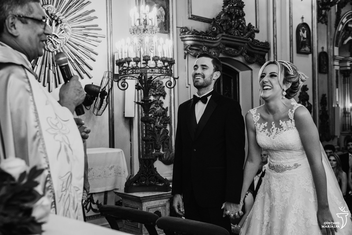 noivos sorrindo de mãos dadas enquanto escutam a missa do padre na cerimônia de casamento na igreja são josé no rio de janeiro
