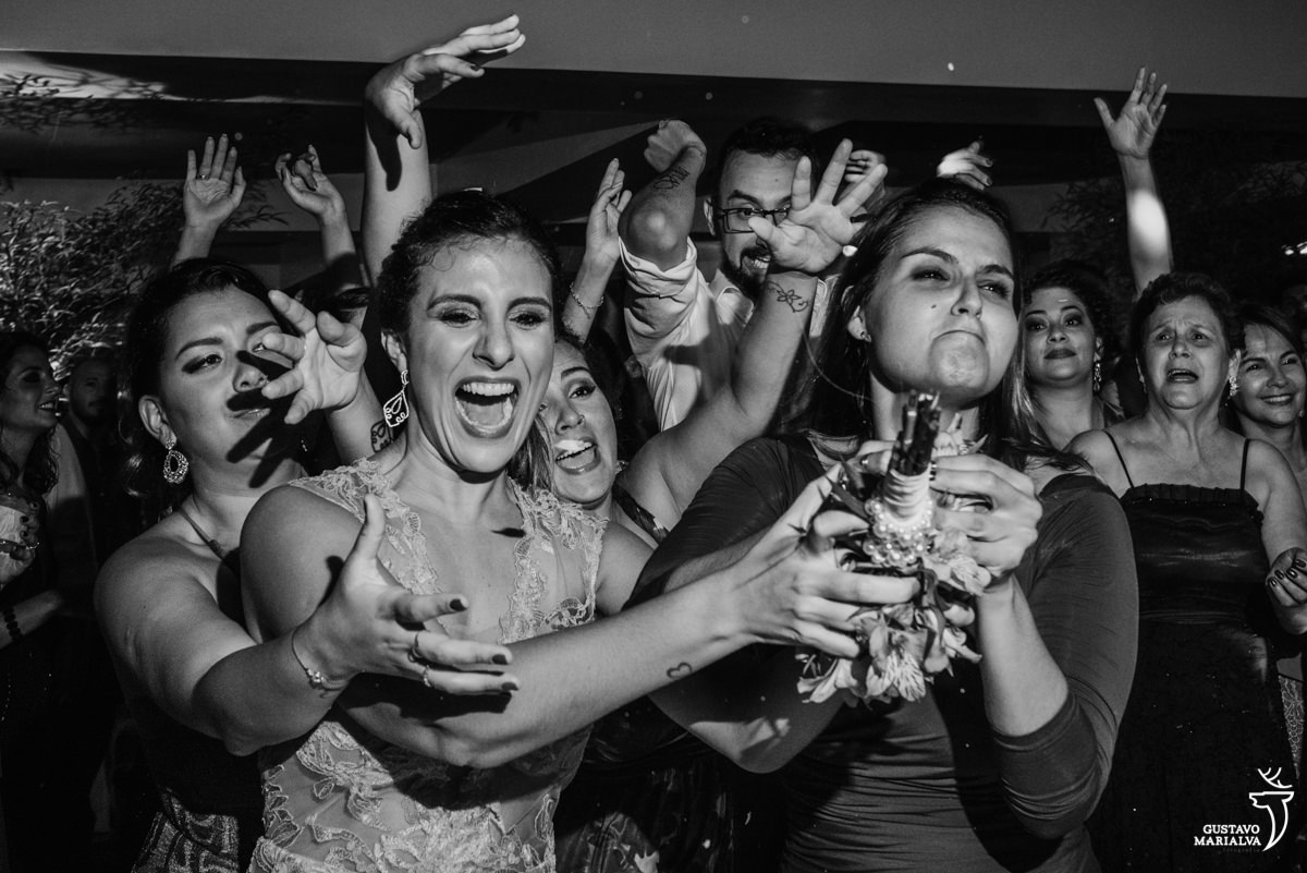 amigas disputam o buquê enquanto outros convidados pulam para tentar pegar