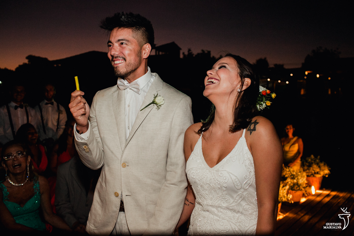 Noivo segurando massinha amarela e sorrindo enquanto a noiva sorri na cerimônia de casamento no Uniq Beach Lounge em Búzios