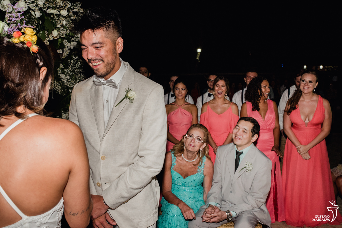 noivo sorri emocionado com os pais e madrinhas ao fundo emocionadas na cerimônia de casamento no Uniq Beach Lounge em Búzios