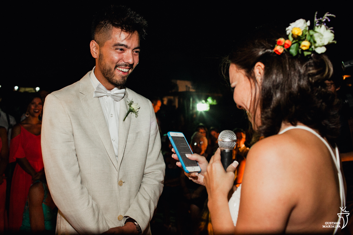 noivo sorri emocionado enquanto a noiva le os votos no celular durante a cerimônia de casamento no Uniq Beach Lounge em Búzios