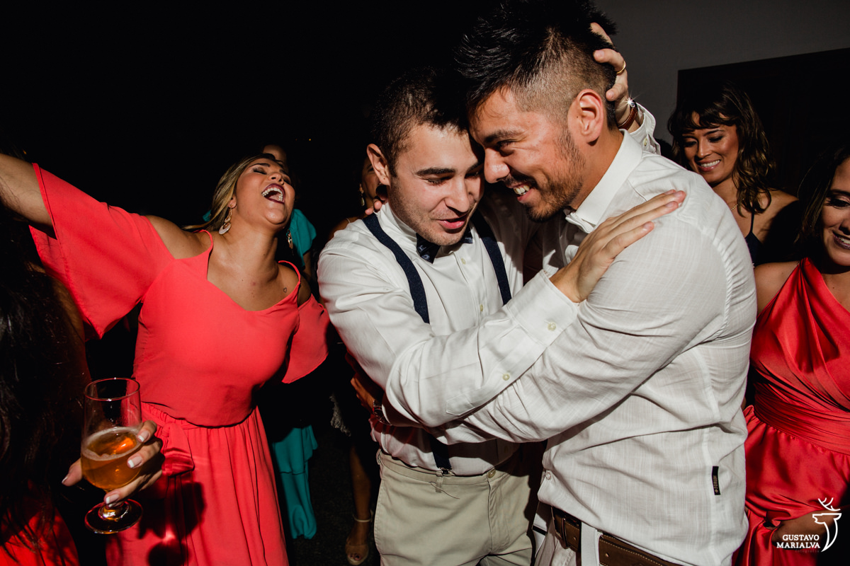 noivo e padrinho se abraçam enquanto madrinha dança na festa de casamento no Uniq Beach Lounge em Búzios