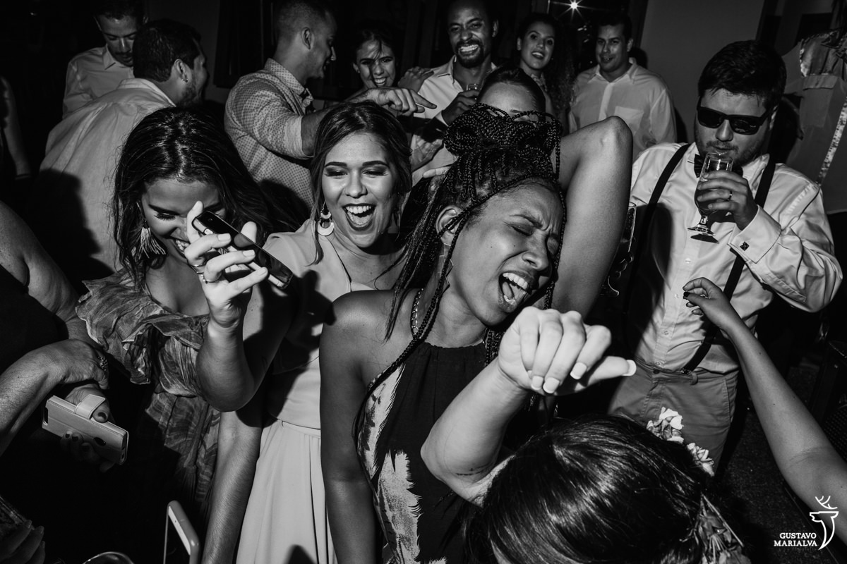 Convidadas dançam funk com a mão na cabeça enquanto padrinho de óculos escuros toma um drink no Uniq Beach Lounge em Búzios