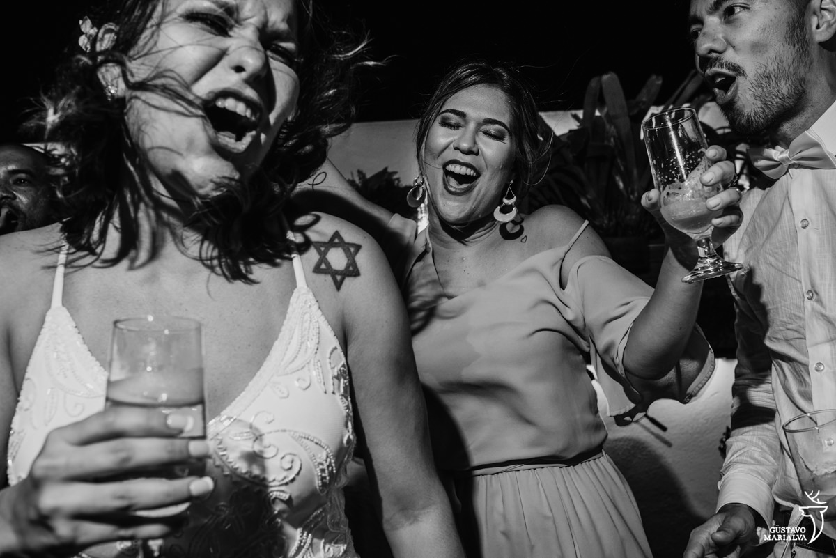 noivos com copo na mão dançam e cantam em cima do palco acompanhados de uma madrinha na festa de casamento no Uniq Beach Lounge em Búzios