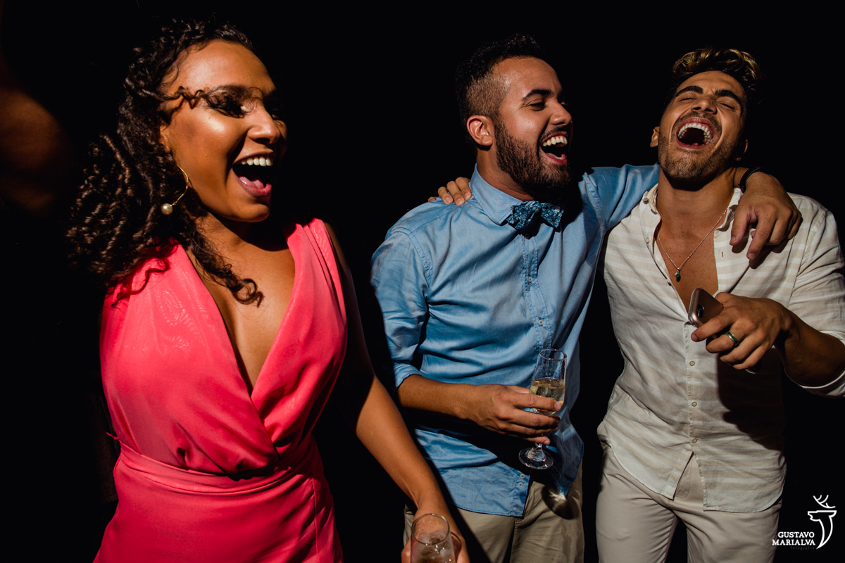 casal de namorados gay dançam animados e abraçados enquanto madrinha dança ao lado na festa de casamento no Uniq Beach Lounge em Búzios