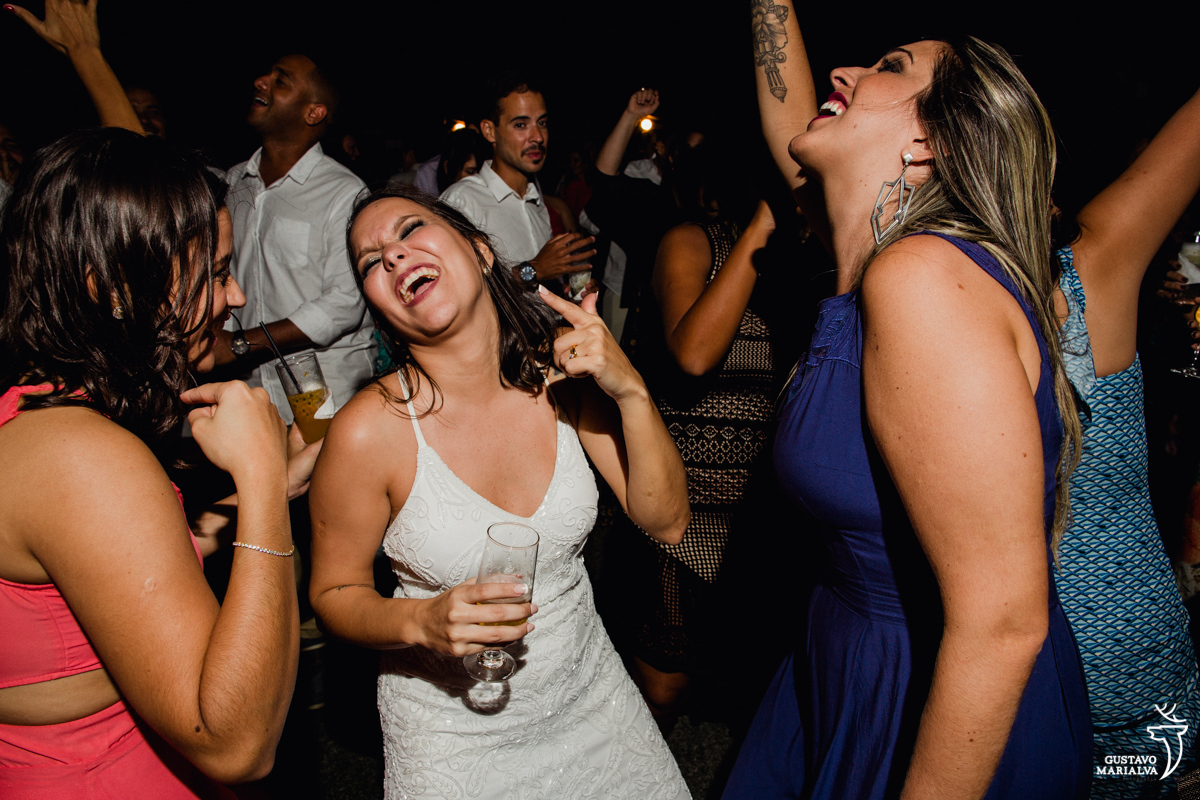 noiva sorrindo com copo na mão dança com as amigas na festa de casamento no Uniq Beach Lounge em Búzios