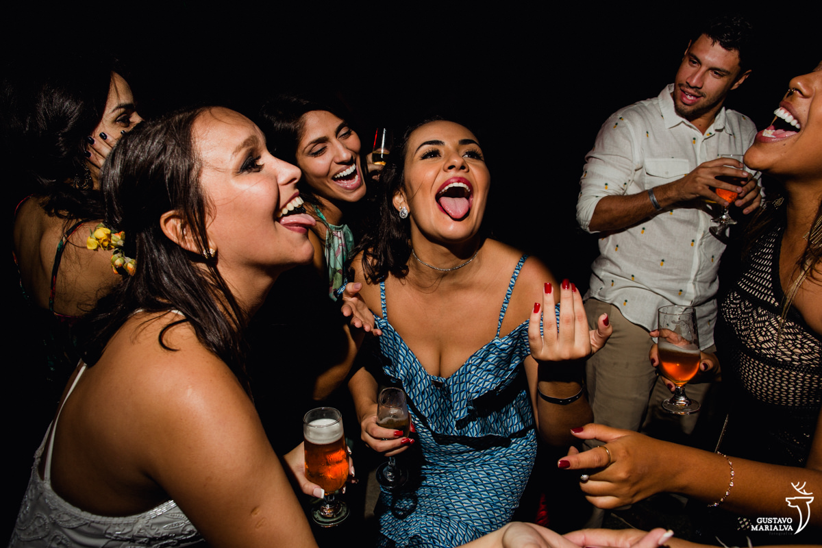 noiva e amiga dançam com a língua para fora e convidado sorri ao fundo