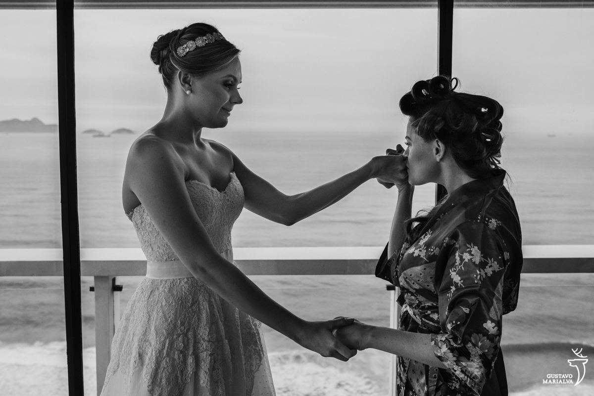 irmã da noiva beijando a mão na noiva enquanto a observa vestida de noiva