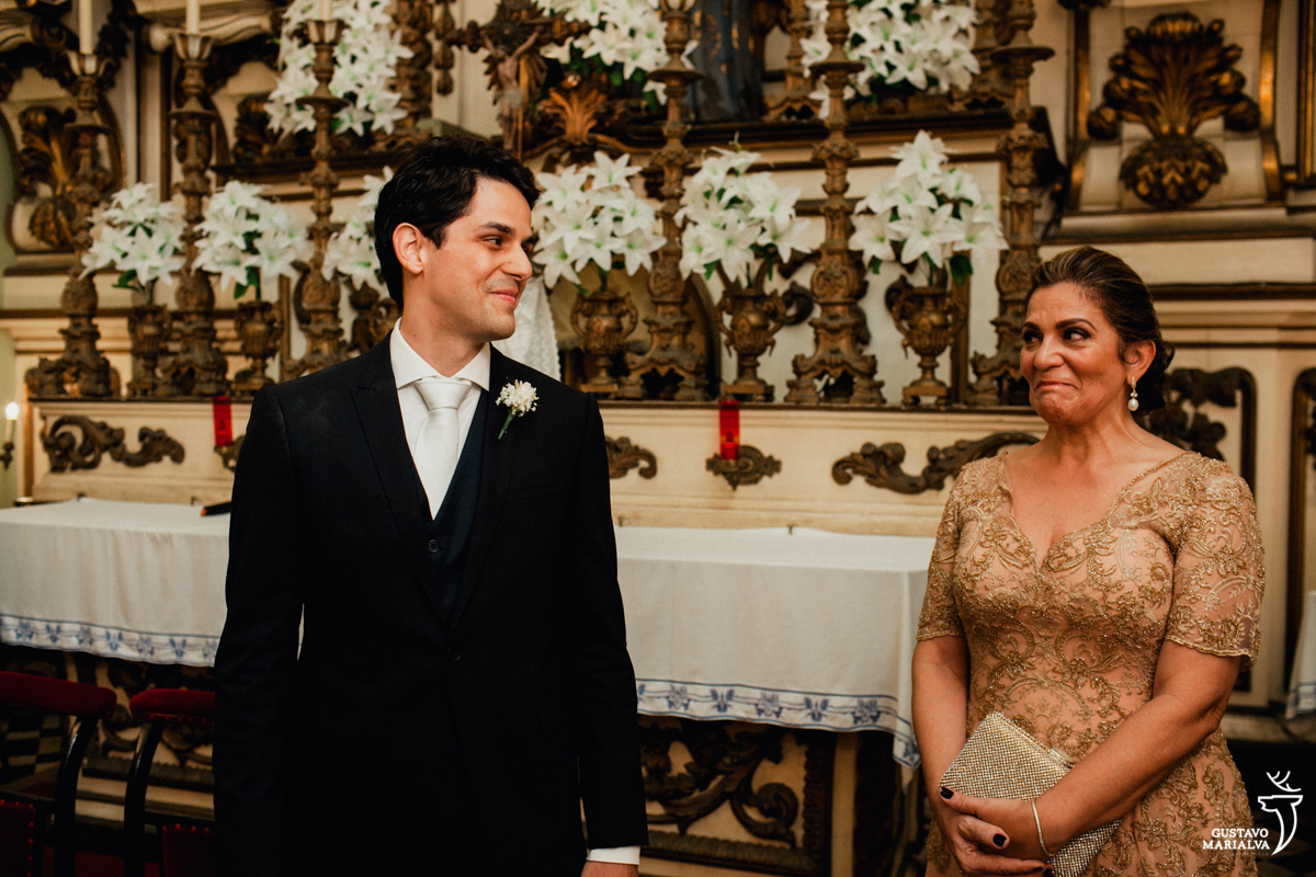 noivo olha sorrindo para mãe emocionada durante a cerimônia de casamento na igreja são josé